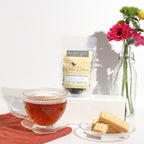 Plum Deluxe Housewarming Blend Black Tea (Vanilla Creme Brulee) in a lifestyle setting, featuring a teacup and loose tea.