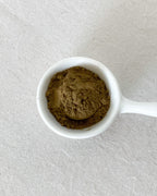 Teappo Iron Goddess Powder in a clear container on a wooden surface, showcasing the powder's texture and color.