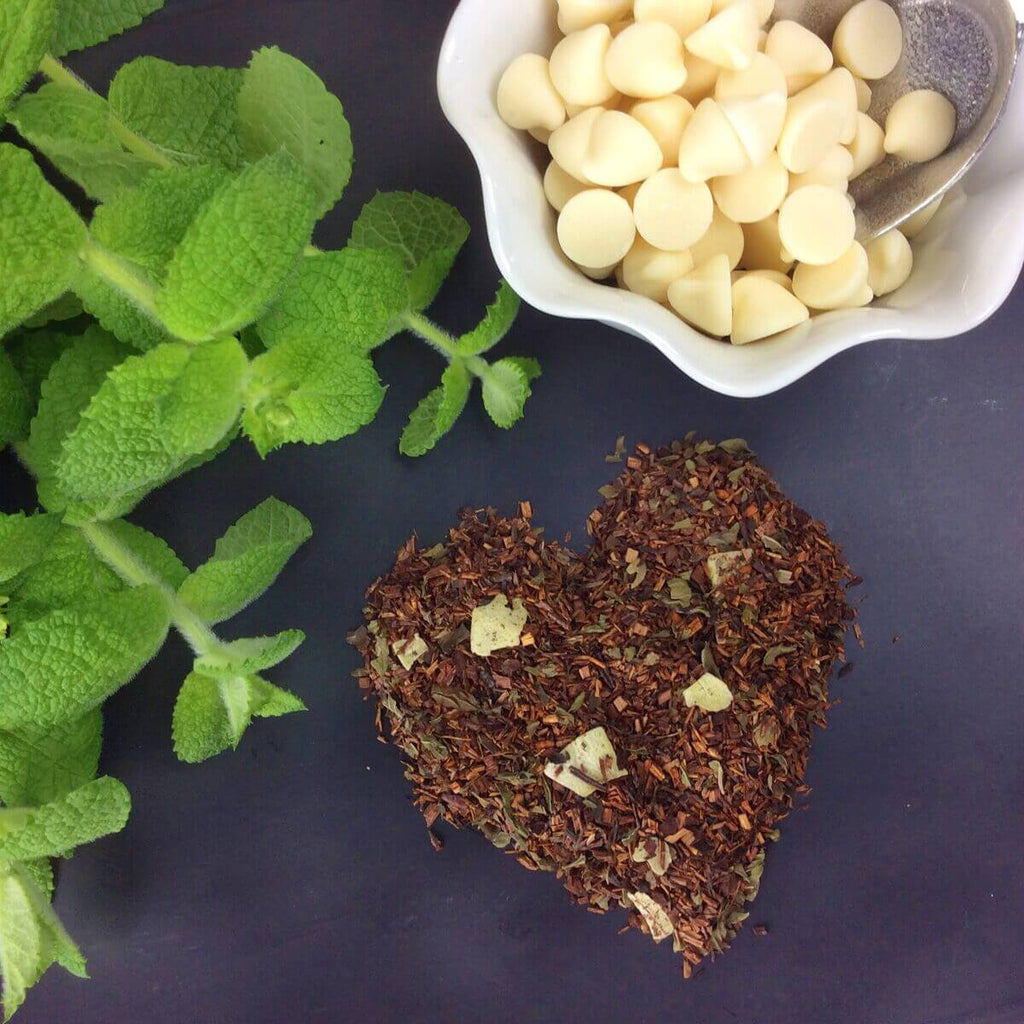 Plum Deluxe White Chocolate Peppermint Herbal Tea packaged in a decorative tin, shown in front of a blurred background.
