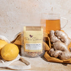 Plum Deluxe Rejuvenation Blend Herbal Tea (Ginger - Lemon) in a cup, with a lemon slice and ginger pieces beside it.