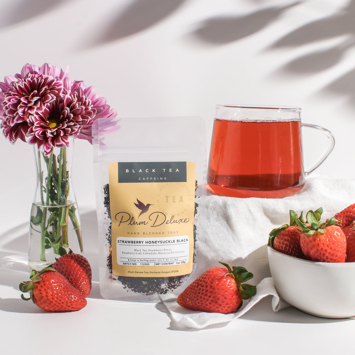Plum Deluxe Strawberry Honeysuckle Black Tea displayed in a cozy lifestyle setting with tea accessories.