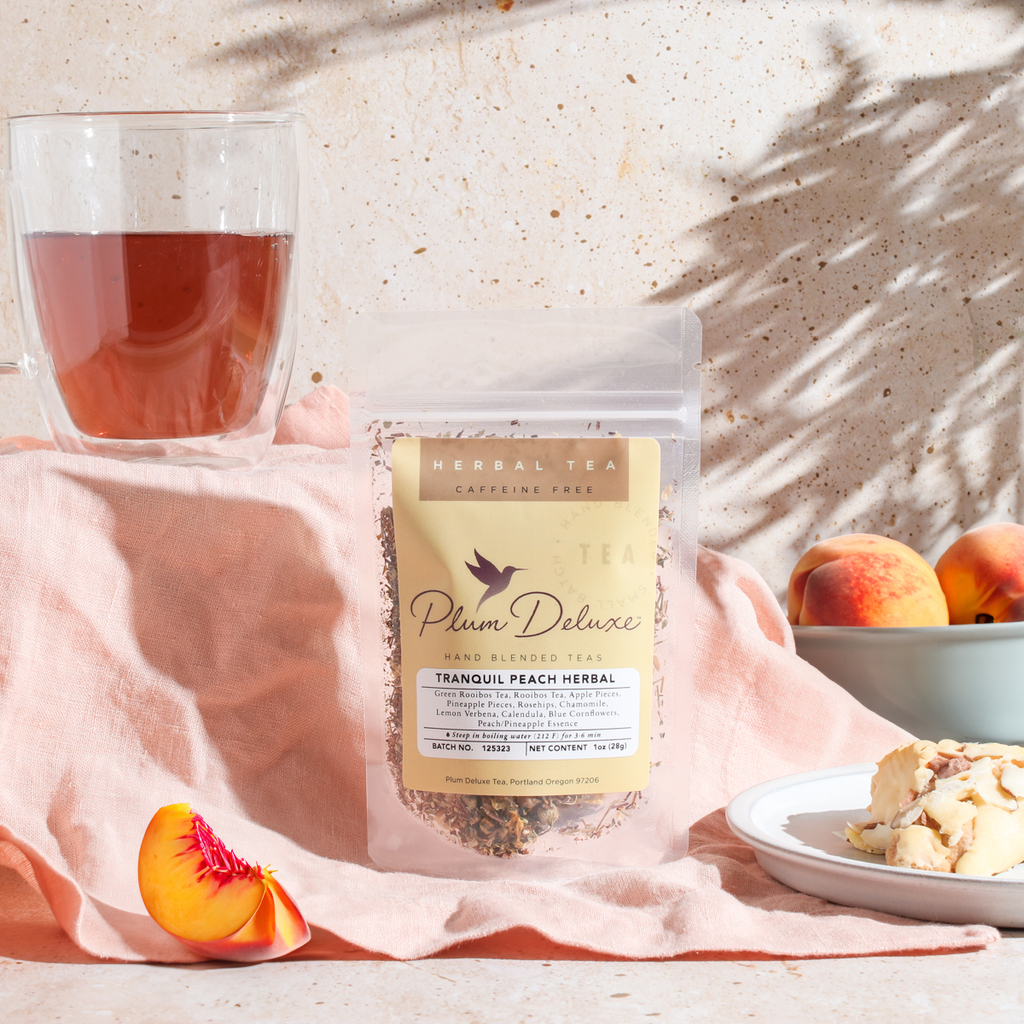 Plum Deluxe Tranquil Peach Herbal Tea with pineapple, peach, and chamomile in a lifestyle setting, shown in a square image.