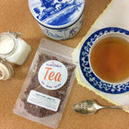 Plum Deluxe Vanilla Creme Herbal Tea loose leaf in a clear glass container, displayed on a wooden surface.