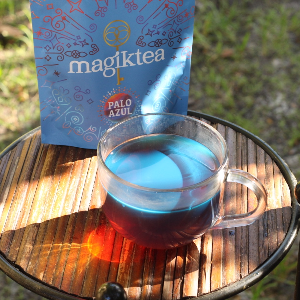 Clear mug with blue liquid next to a 'magiktea' package on a wooden surface.