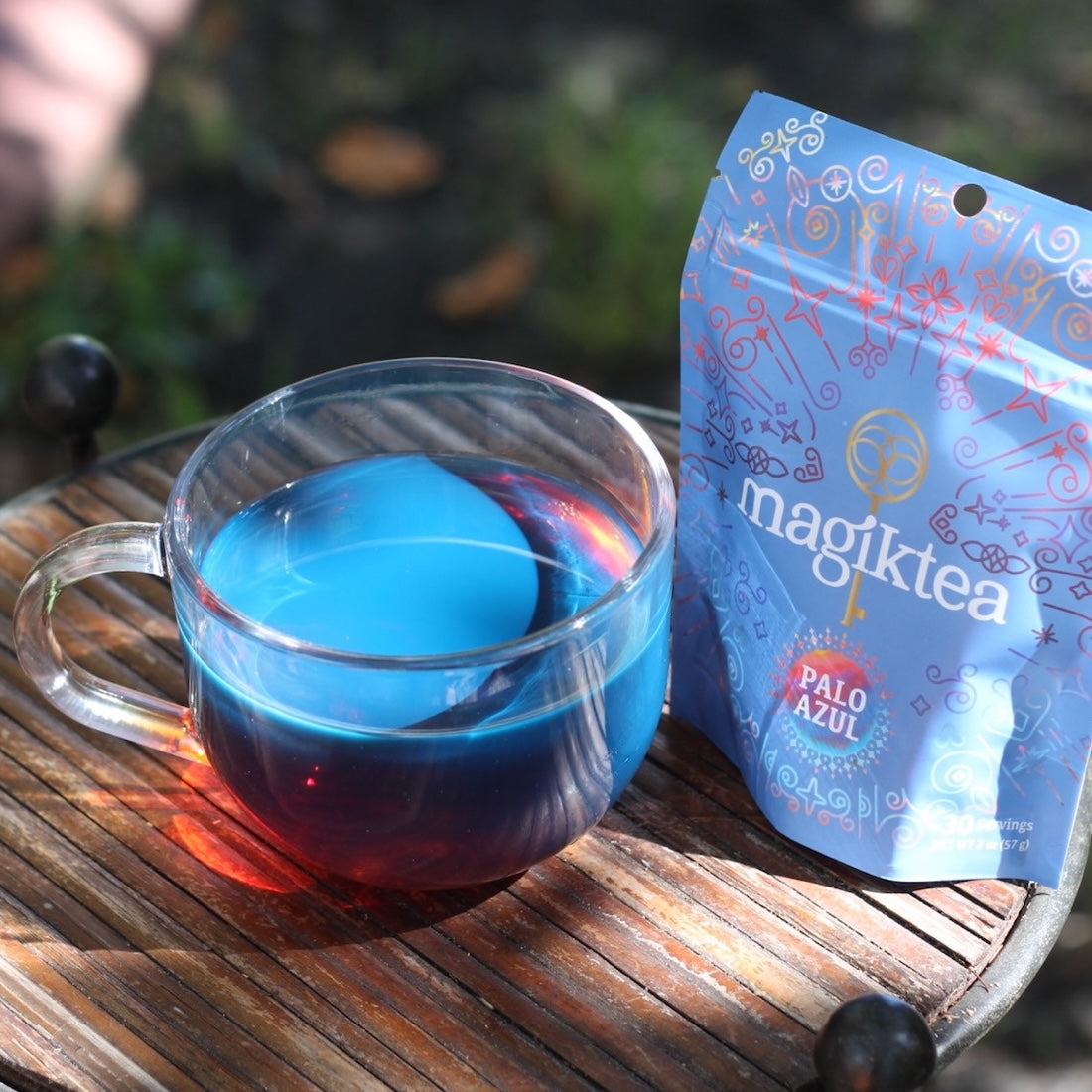 Clear mug with blue liquid and 'magiktea' packaging on a wooden surface